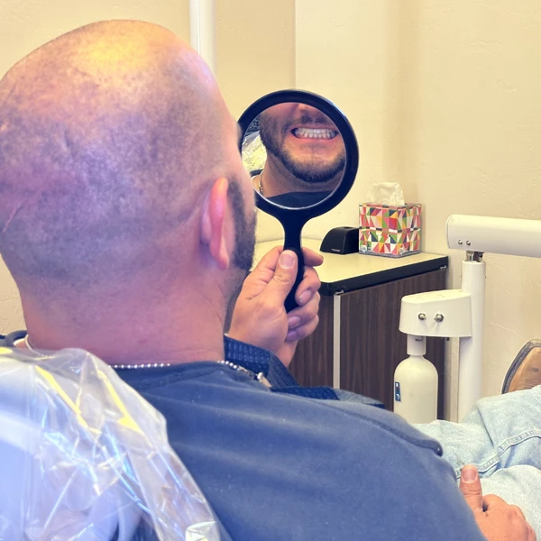 A patient holding a hand mirror and smiling at their reflection